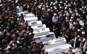 Druze elders and mourners surround the coffins of 10 of the 12 people killed in a rocket strike from Lebanon a day earlier, during a mass funeral in the Druze town of Majdal Shams in the Israel-annexed Golan Heights, on July 28, 2024. The Israeli military said the victims were struck by an Iranian-made rocket carrying a 50-kilogram warhead that was fired by Lebanese Hezbollah group at a soccer field in the Druze Arab town. Hezbollah has denied responsibility for the strike. (Photo by Jalaa MAREY / AFP)