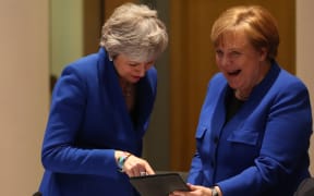 Theresa May and Angela Merkel share a laugh over something on a tablet during the crunch summit in Brussels.