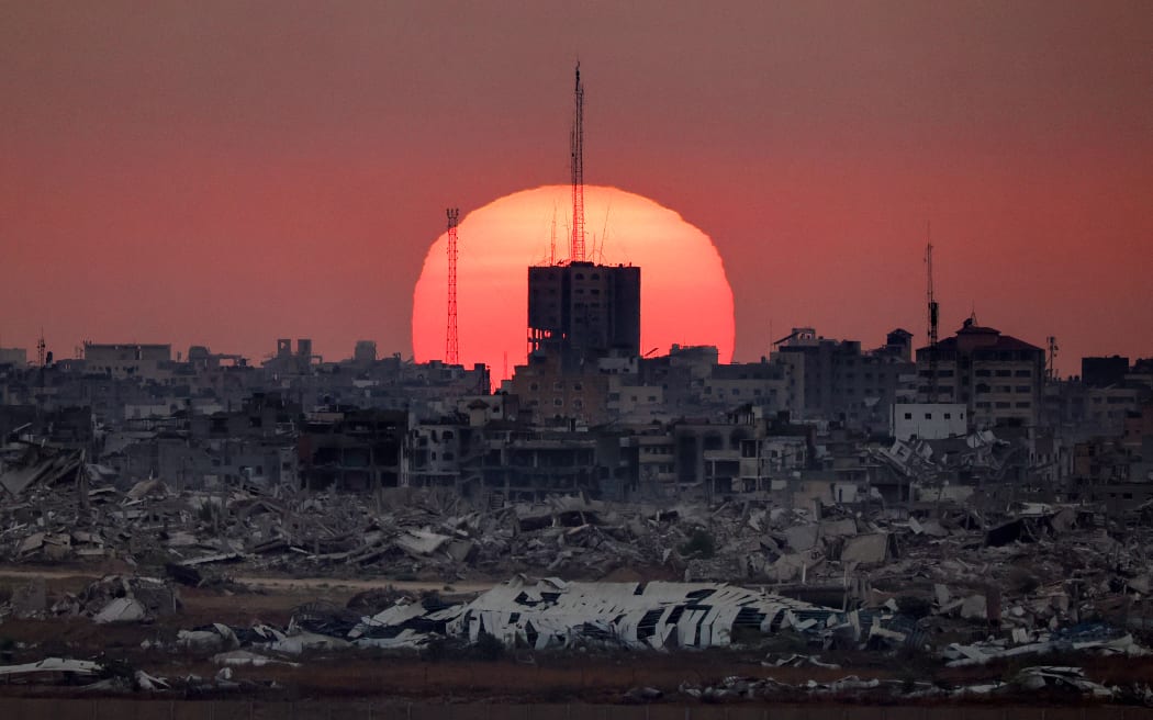 This picture taken from a position on the Israeli border with the Gaza Strip, shows the sun setting behind destroyed buildings in the Palestinian territory, on July 1, 2025. (Photo by Jack GUEZ / AFP)
