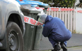 A police investigator looks closely at a set of rubbish bins on Renall St