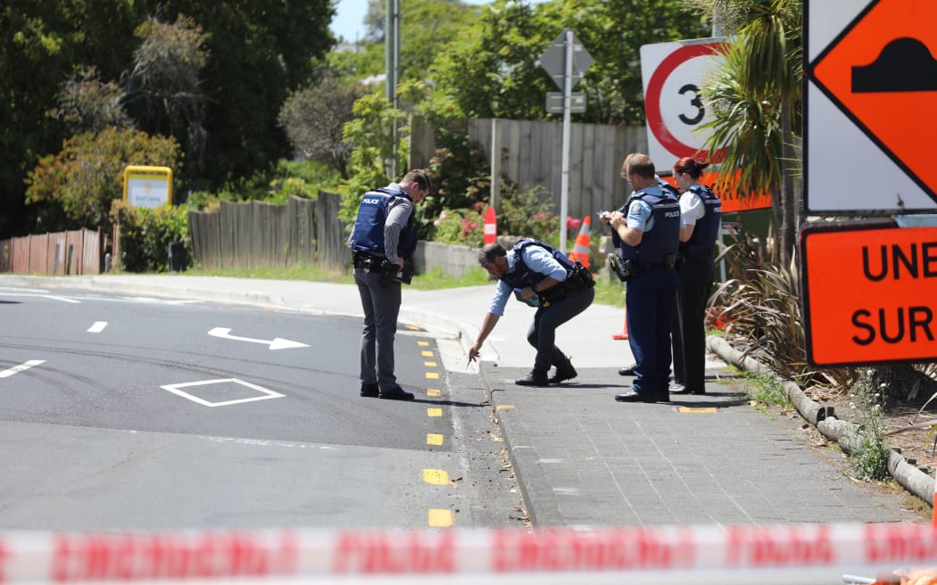 Lights are out at Birkenhead Ave intersection with Onewa Road and traffic is being manually directed by a person in a high-vis vest while armed police guard a cordon.