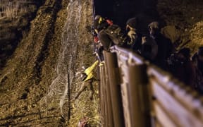 A Central American migrant jumps over the US-Mexico border fence from Tijuana to San Diego in the US