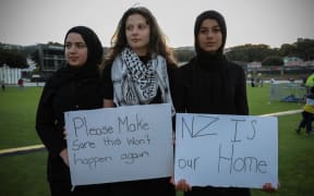 Three young women and their signs at the Basin Reserve vigil in Wellington  for the victims of the Christchurch terror attack