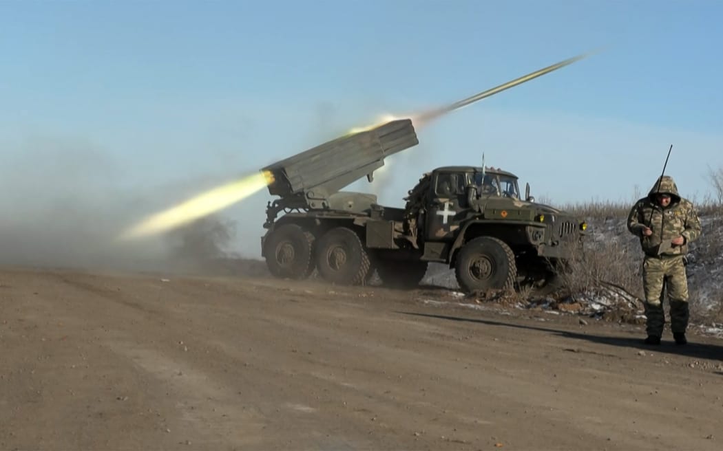 This grab taken from AFP video footage shows a member of Ukraine's military looking away as a BM-21'Grad' MLRS 122mm rocket launcher fires on the outskirts of Soledar on January 11, 2023. - Ukrainian President Volodymyr Zelensky has said fighting is still raging in a key eastern frontline city that a Russian mercenary group earlier said it controlled, as Moscow announced a new military commander in Ukraine. The fate of Soledar in eastern Ukraine was uncertain after Russian group Wagner claimed it controlled the gateway town -- but the Kremlin cautioned against declaring victory prematurely.