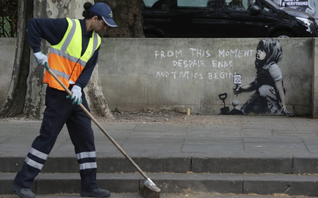 A road worker passes by an artwork which appears to be by street artist Banksy which has appeared near the former location of the Extinction Rebellion camp in Marble Arch, London, Friday April 26, 2019.