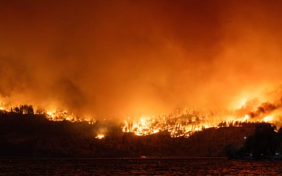 The McDougall Creek wildfire burns in the hills West Kelowna, British Columbia, Canada, on August 17, 2023, as seen from Kelowna. Evacuation orders were put in place for areas near Kelowna, as the fire threatened the city of around 150,000. Canada is experiencing a record-setting wildfire season, with official estimates of over 13.7 million hectares (33.9 million acres) already scorched. Four people have died so far. (Photo by Darren HULL / AFP)