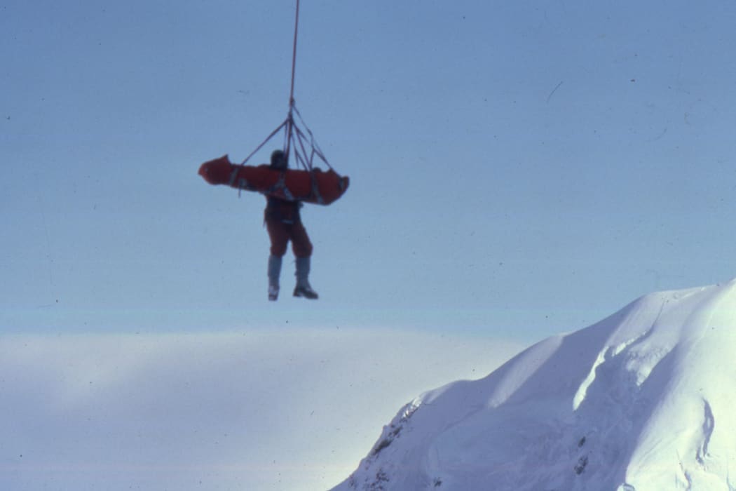 A photo of Don Bogie hanging from the helicopter with Mark Inglis attached to him in a soft stretcher known as a Bauman Bag