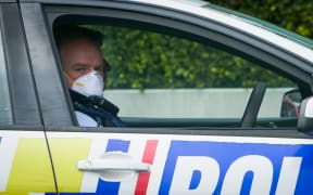 An Auckland Police officer sitting in his car wearing a mask looking at the camera. Covid 19