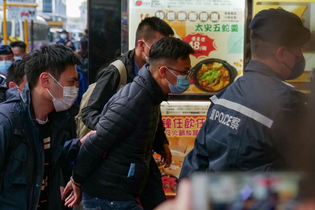 Stand News chief editor Patrick Lam (C) is brought to the news outlet's office building in handcuffs after police were deployed to search the premises in Hong Kong's Kwun Tong district on 29 December 2021.
