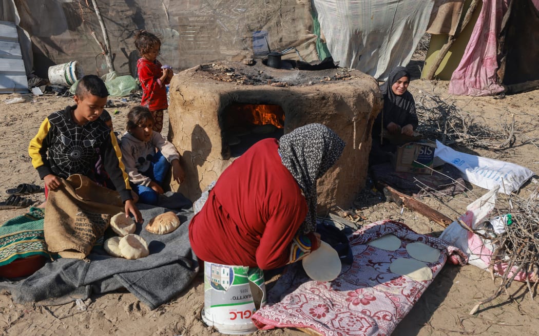 A displaced Palestinian woman and children who fled Khan Yunis, cook breakfast in Rafah further south near the Gaza Strip's border with Egypt, on December 6, 2023, amid continuing battles between Israel and the Palestinian militant group Hamas. Israeli forces were encircling southern Gaza's main city of Khan Yunis on December 6, 2023, battling Hamas militants through streets and buildings in some of the most intense combat of the two-month war.