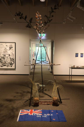 The artwork features a surveyor's tripod made from flax stalks to symbolise Māori reclamation of their land.