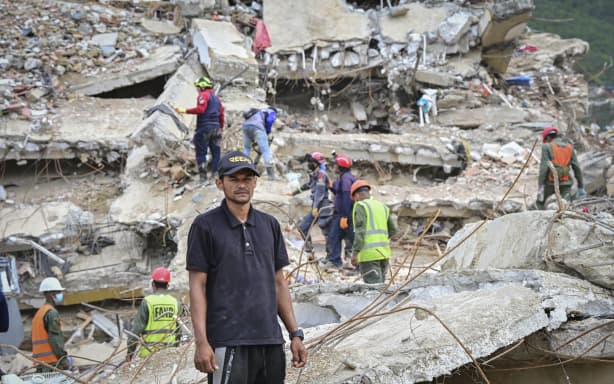 Miguel Baez, a volunteer rescuer, stands outside the collapsed apartment building where his family lived as he and relatives search for family members believed to be trapped inside, in Caraballeda, La Guaira state, Venezuela, on July 12, 2026. The twin earthquakes that struck Venezuela on June 24 had left nearly 4,500 people dead as of July 12, while much of the affected population continued to live in camps, according to official figures. (Photo by MARTIN BERNETTI / AFP)