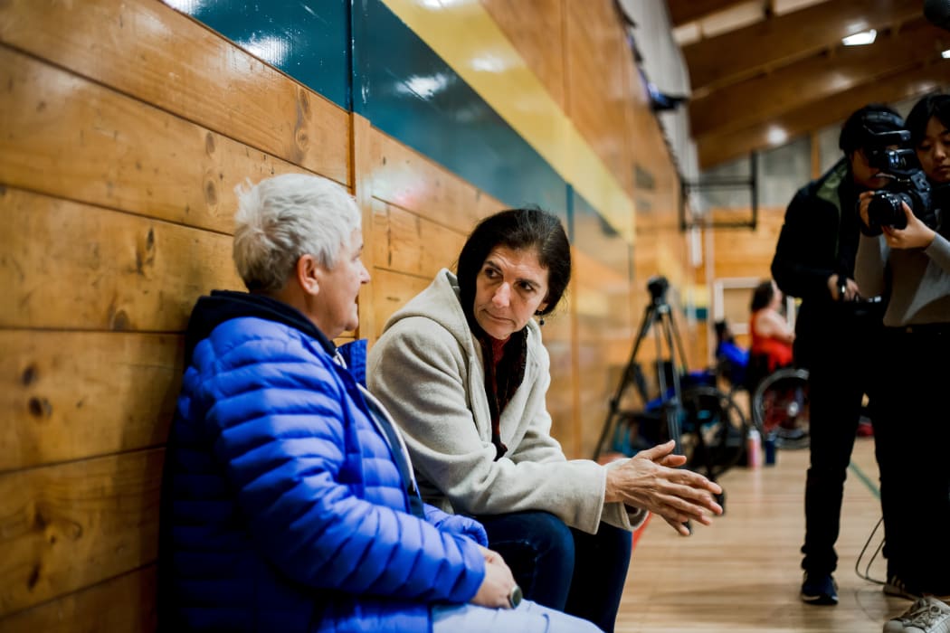 Nadmea sits down and talks with a friend at a wheelchair basketball game