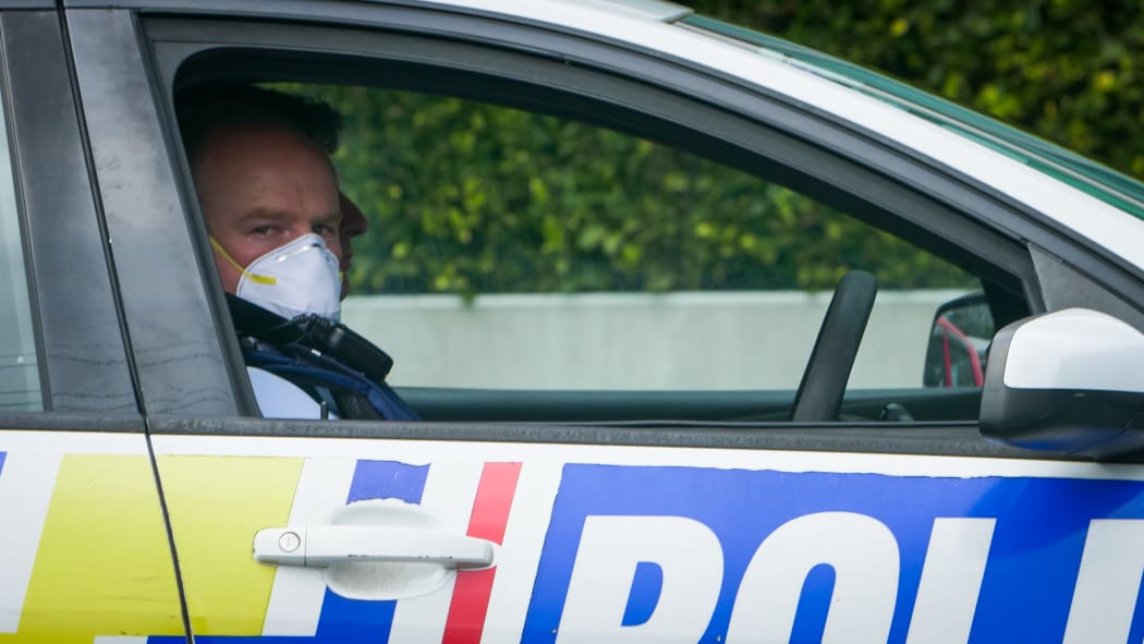 An Auckland Police officer sitting in his car wearing a mask looking at the camera. Covid 19