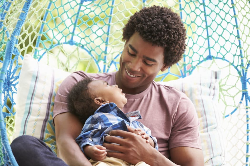 A photo of a father with baby son relaxing on outdoor garden swing seat