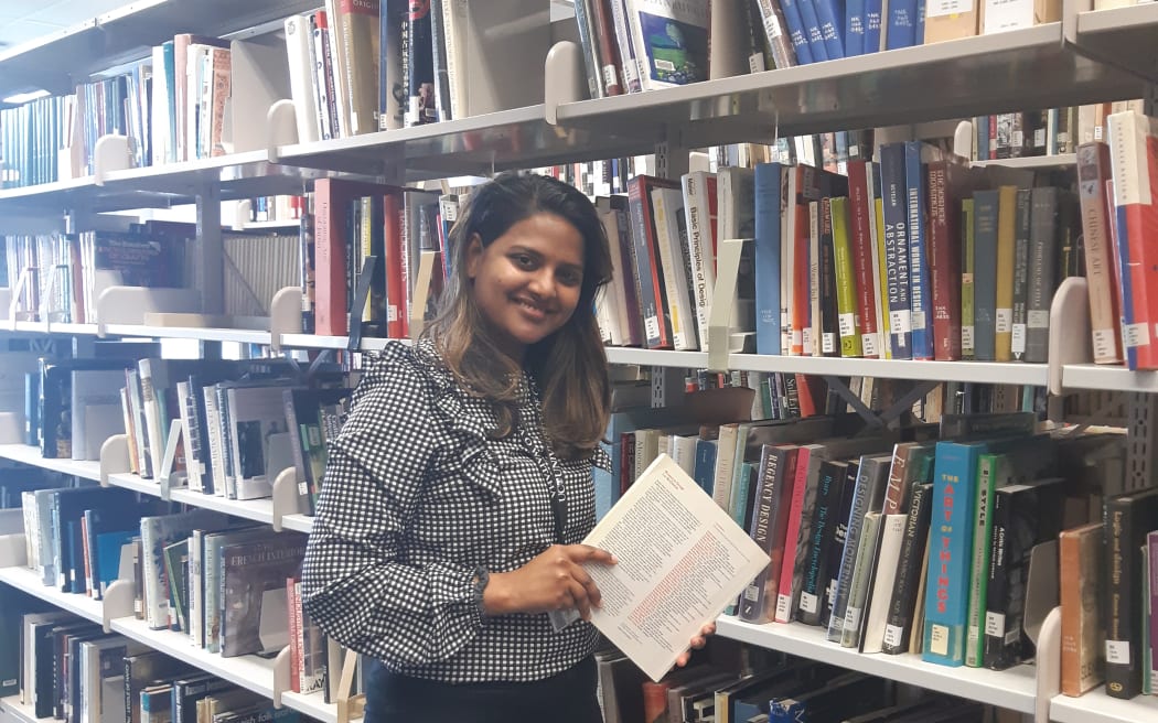 International PdD student Himasha Gunasekara in front of a library bookshelf.