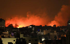 Buildings in Gaza City are lit up by fire and smoke from an Israeli air strike, on 8 October, 2023.