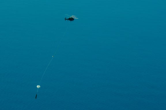 A helicopter carrying a big cylinder on a line.