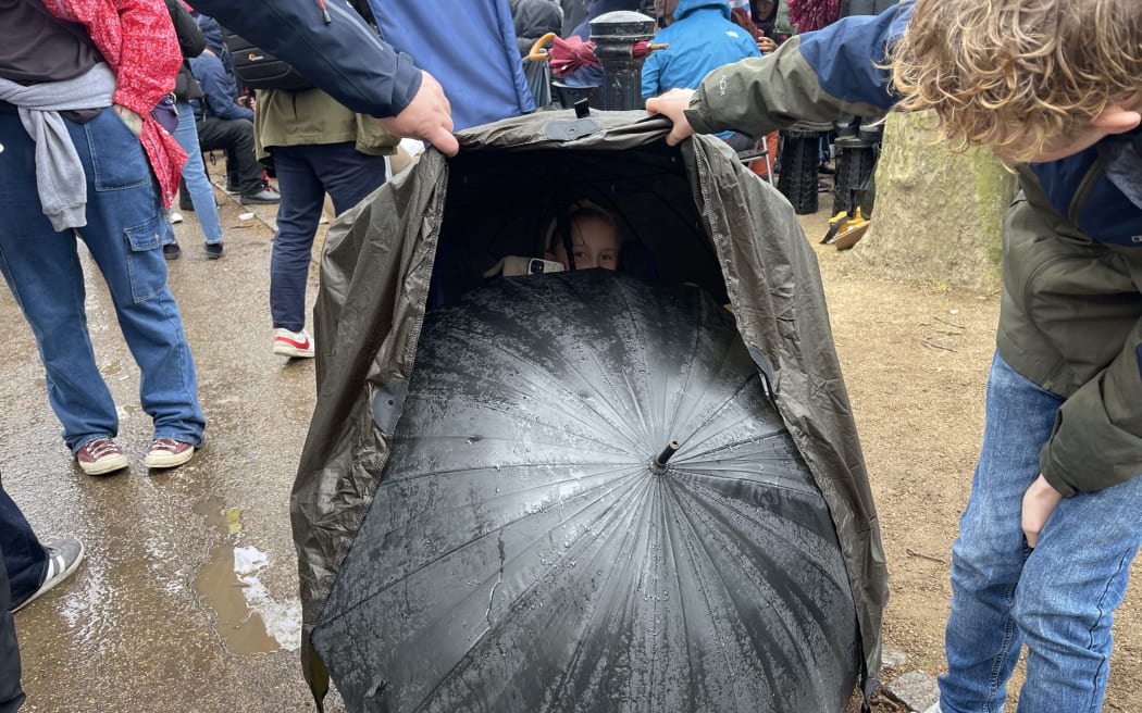 The crowd is coming up with clever ways to avoid the rain at the procession.