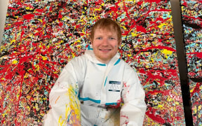 Ed Sheeran poses in front of his paintings created at an abandoned London car park.