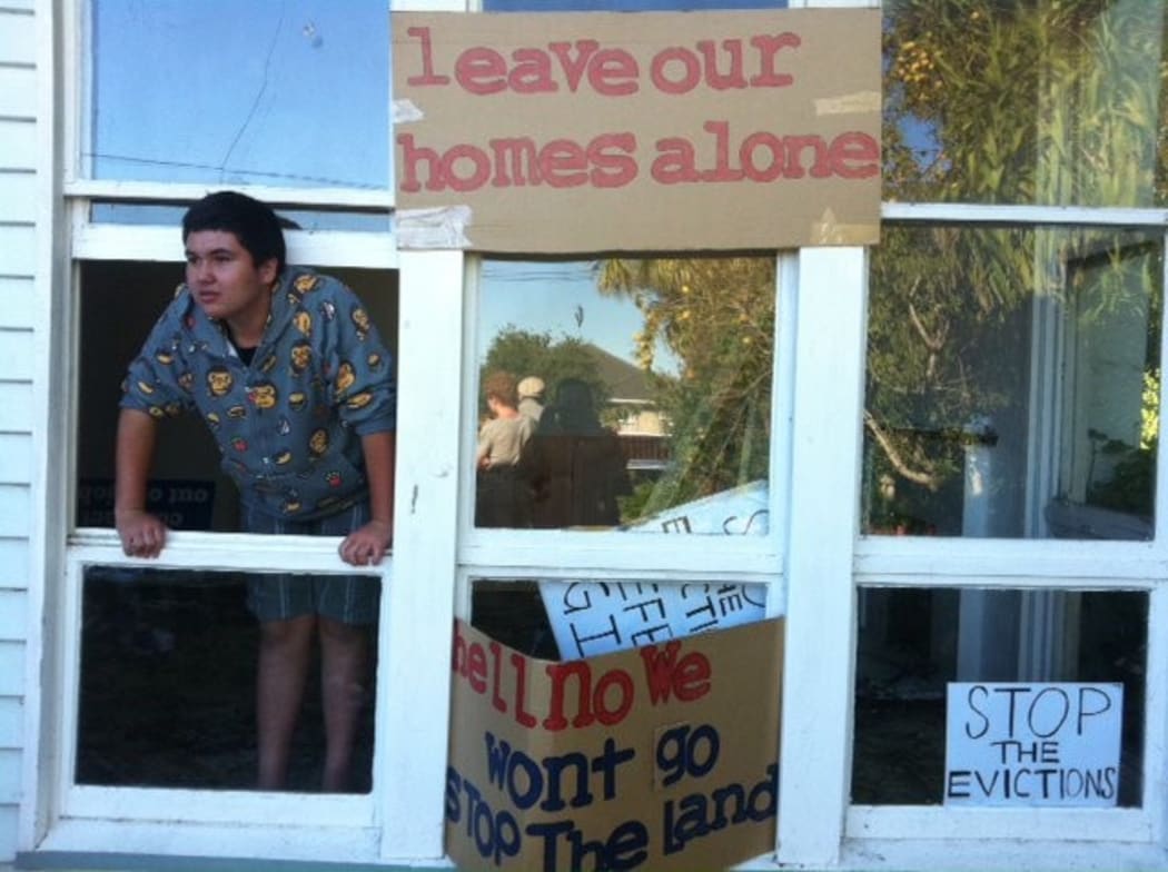Scott Hita perches in the window of a house surrounded by placards