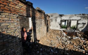 Olga, 67, looks at her house destroyed by shelling in the village of Moshchun, Kyiv region, 28 July 2022, amid the Russian military invasion of Ukraine.