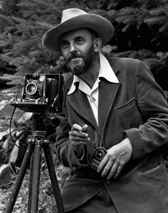A black and white image of Ansel Adams with his camera