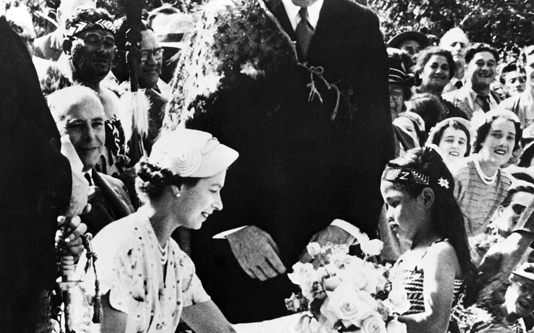 A little girl offers flowers at a welcoming ceremony in honour of Queen Elizabeth II (left), on 6 January, 1954 in Waitangi, during her visit in New Zealand.