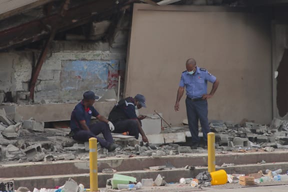 Police work at the site of a damaged building in Port Moresby on January 12, 2023. Troops patrolled the streets of Papua New Guinea's capital on January 12, under a state of emergency following riots that killed 16 across the country's two largest cities. (Photo by AFP)