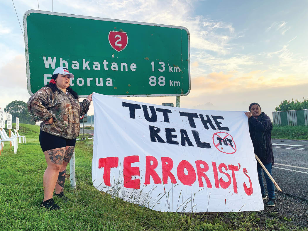 Talei Bryant (L) and another woman work to hang a hand-painted sheet over a road sign outside Te Uru Taumatua offices in Tāneatua.