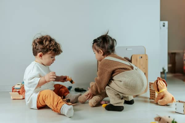 Two young children play together in a white room.