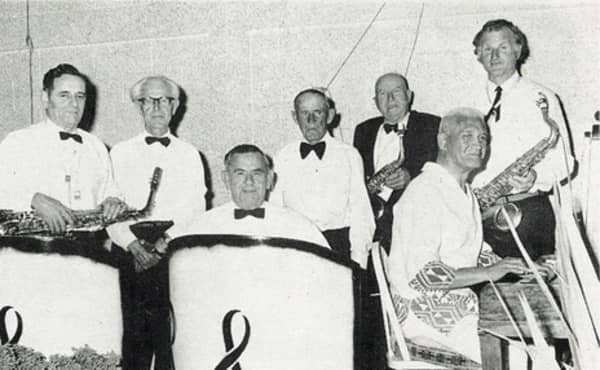 Seven older men dressed in white shirts hold musical instruments.