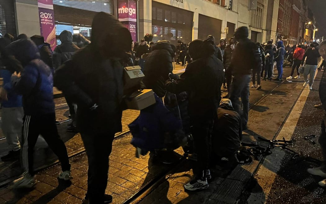 Protestors sort through looted goods in Dublin on November 23, 2023, as people took to the streets in protest following the stabbings earlier in the day. Protesters in Dublin on Thursday torched a car and fought police, an AFP journalist reported, after three children were injured in a suspected school stabbing that social media rumours attributed to a foreign national. (Photo by Peter MURPHY / AFP)