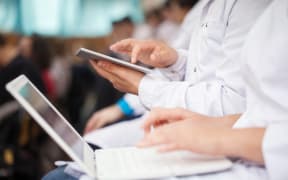 Male and female medical students or doctors using digital tablet and laptop during the lecture or conference. Focus on the man with pad