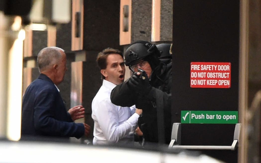 Two hostages run for cover behind a policeman.