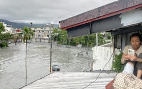 A resident uses her mobile phone while sitting on the roof of a house, as water from a burst landslide dam overflows and floods the area in Hualien on September 23, 2025, as a result of heavy rain due to Super Typhoon Ragasa. The super typhoon was generating maximum sustained winds of 220 kilometres (137 miles) per hour near its centre while moving west across the South China Sea, according to Hong Kong's weather service.