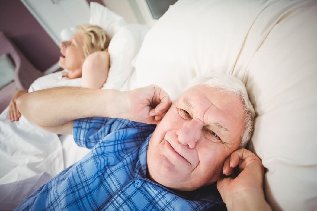 Senior man covers ears while wife snores