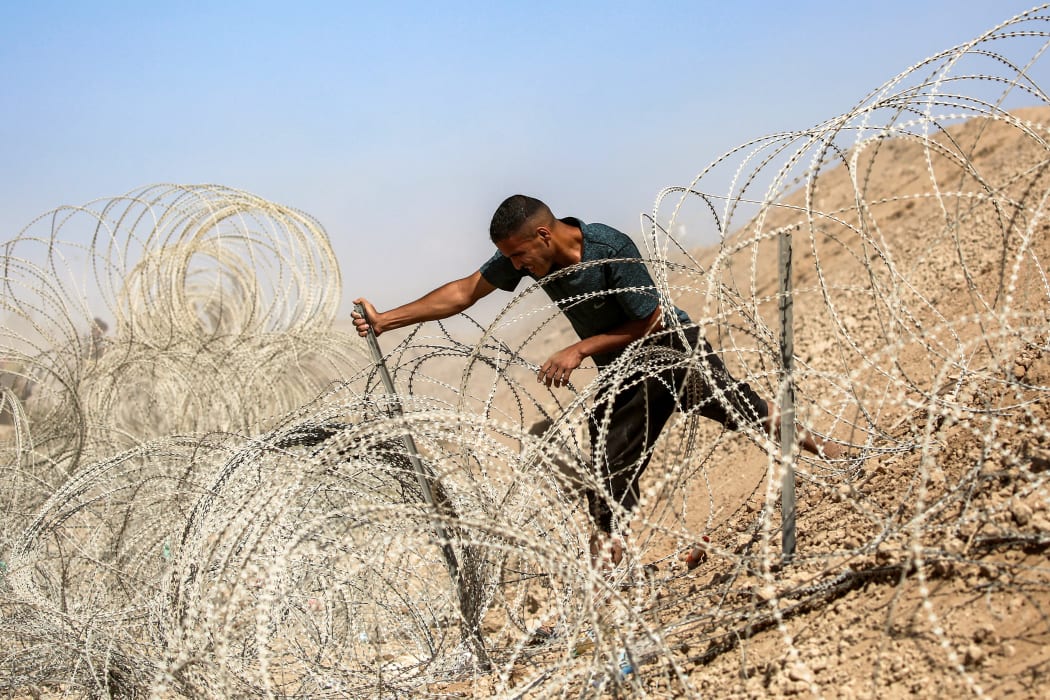 A man attempts to remove parts of the barbed-wire fence at the so-called "Netzarim corridor" near Nuseirat in the central Gaza Strip on October 10, 2025, as people make their way back to Gaza City. Gaza's civil defence agency said on October 10 that Israeli forces have begun pulling back from parts of the territory, particularly in Gaza City and Khan Yunis. Israeli prime minister's office said that the government had "approved the framework" of a hostage release deal with Hamas, as both sides edged closer to ending more than two years of hostilities in Gaza. (Photo by Eyad BABA / AFP)