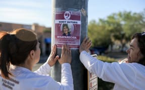 TUCSON, ARIZONA - FEBRUARY 24: Rachel Navarro (L) and Lidia Hernandez, who are part of the Madres Buscadoras De Sonora (Searching Mothers of Sonora), place a flyer that reads, 'Nancy Guthrie Desparecida' (Disappeared) on a pole about a mile from Nancy Guthrie's residence on February 24, 2026, in Tucson, Arizona. The organization is dedicated to finding lost people in the Mexican state of Sonora and, sometimes, in other areas. Law enforcement officials continue to search for Nancy Guthrie, the 84-year-old mother of U.S. journalist and television host Savannah Guthrie, after she went missing from her home on the morning of February 1st. Savannah Guthrie announced a $1 million reward for anyone who helps find her mother.   Joe Raedle/Getty Images/AFP (Photo by JOE RAEDLE / GETTY IMAGES NORTH AMERICA / Getty Images via AFP)