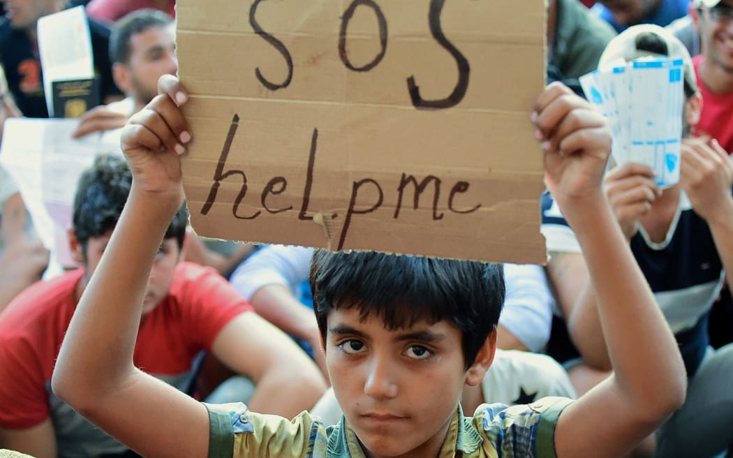A migrant boy holds a sign reading "SOS help me" as he sits with other migrants in front of the railway station in Budapest.