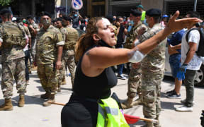 An injured Lebanese anti-government protester reacts as members of the security forces stand guardin the Gemayzeh neighbourhood during the visit of French President Emmanuel Macron on August 6, 2020, two days after a massive explosion in the Beirut port shook the capital.