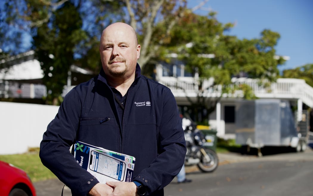 Compliance Manager Adrian Wilson stands in the middle of a street holding documents.