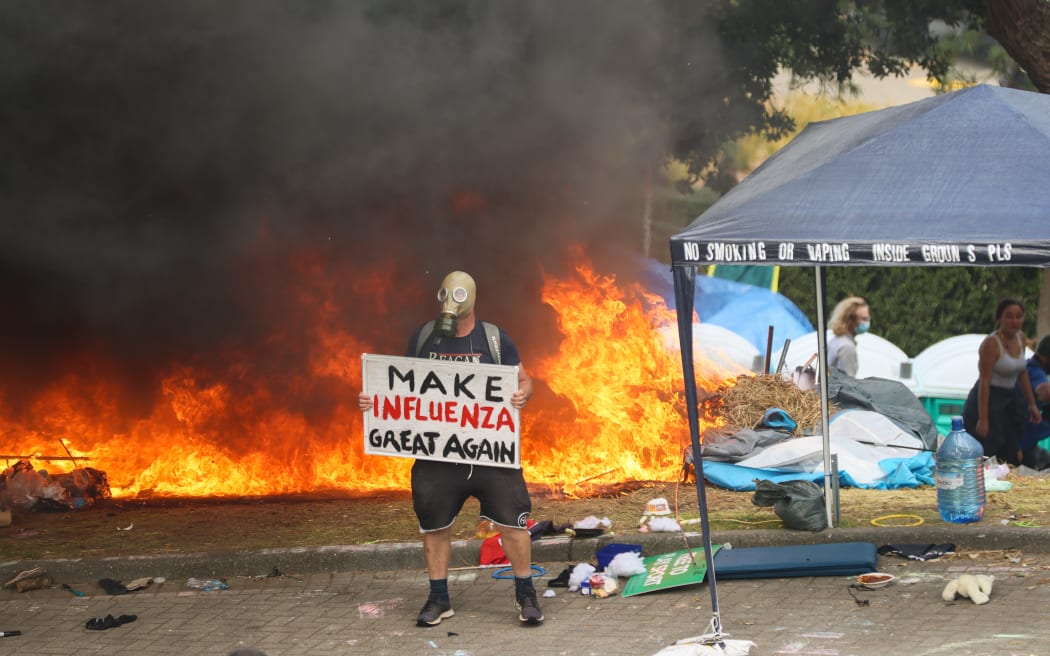 A protest stands in front a fire with a puzzling sign.