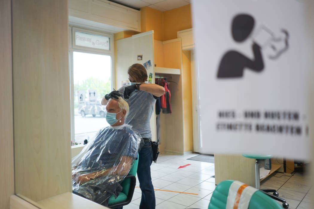 A Berlin hairdresser cuts the hair of a regular customer in his salon, while a notice on the mirror indicates that hygiene rules must be observed.