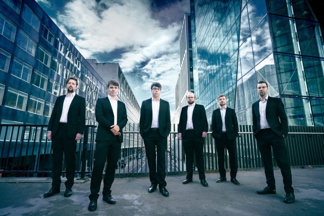 Gesualdo Six in black suits against a blue & white cityscape