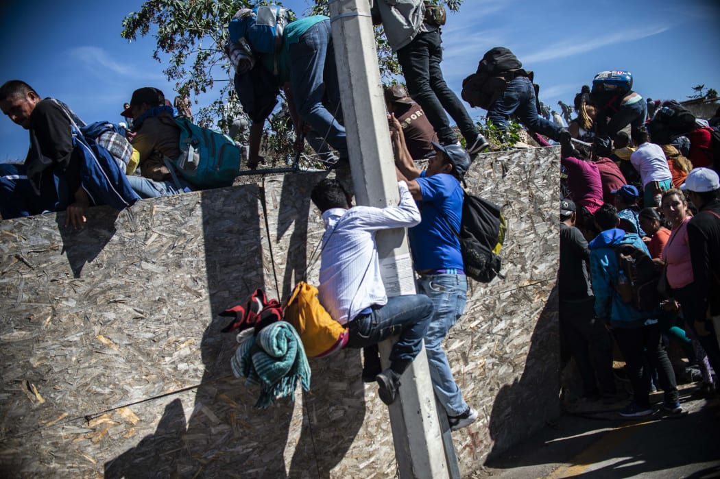 A group of Central American migrants - mostly from Honduras - get over a fence as they try to reach the US-Mexico border.