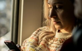 A blonde woman in soft light looks down at her phone.