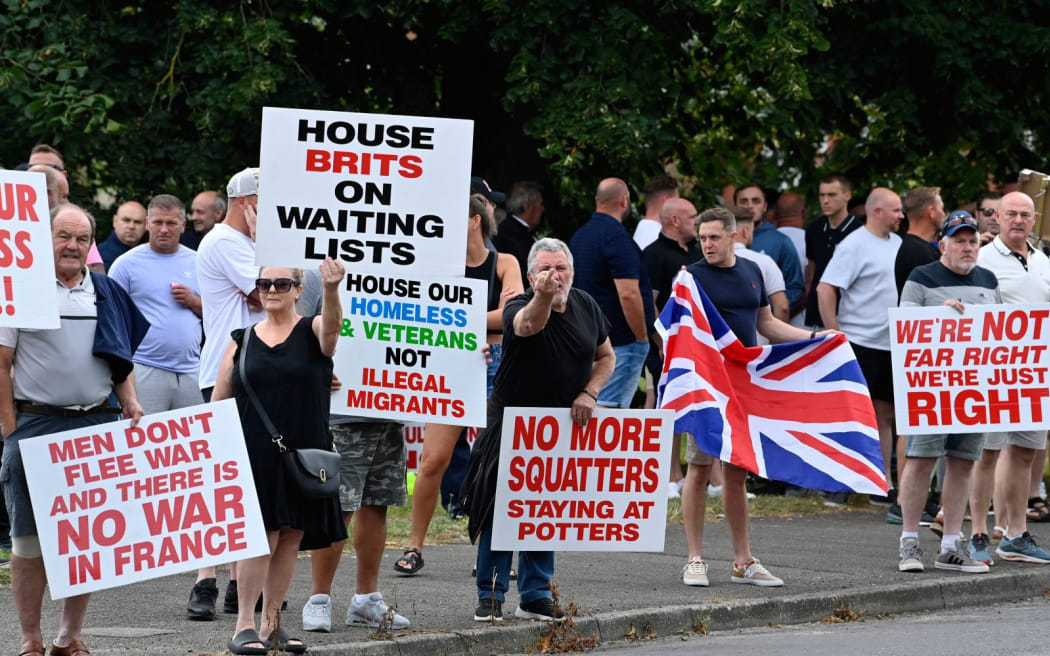 Protesters hold placards during a 'Enough is Enough' demonstration called by far-right activists near a hotel housing asylum seekers in Aldershot on August 4, 2024. Far-right protesters clashed with British police during tense rallies as unrest linked to disinformation about a mass stabbing that killed three young girls spread across the UK. (Photo by JUSTIN TALLIS / AFP)