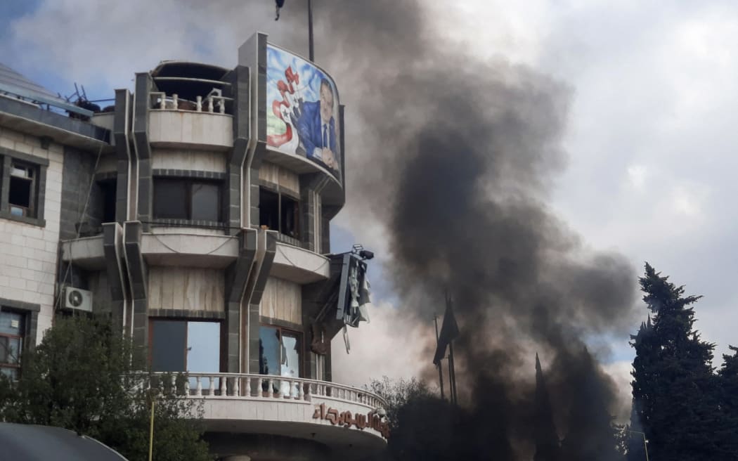 A handout picture released by the Suwayda 24 news site shows smoke billowing during a rally to protest deteriorating living conditions in front of the Suwaida (also known as Sweida) governorate building in the southern Syrian city, on 4 December 2022. - A protester and a policeman were killed Sunday in Syria's southern city of Sweida as security forces cracked down on a rare demonstration by hundreds against deteriorating living conditions.