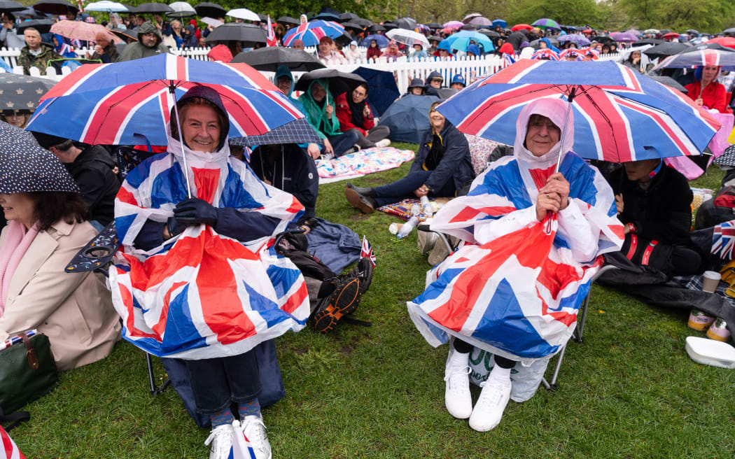 Well-wishers protect themselves against the rain as they wait along the route of the 'King's Procession', a two kilometres stretch from Buckingham Palace to Westminster Abbey, as they wait for Britain's King Charles III and Britain's Camilla, Queen Consort to pass in the Diamond State Coach, in central London, on May 6, 2023 ahead of their coronations. - The set-piece coronation is the first in Britain in 70 years, and only the second in history to be televised. Charles will be the 40th reigning monarch to be crowned at the central London church since King William I in 1066. Outside the UK, he is also king of 14 other Commonwealth countries, including Australia, Canada and New Zealand. Camilla, his second wife, will be crowned queen alongside him and be known as Queen Camilla after the ceremony. (Photo by Niklas HALLE'N / AFP)
